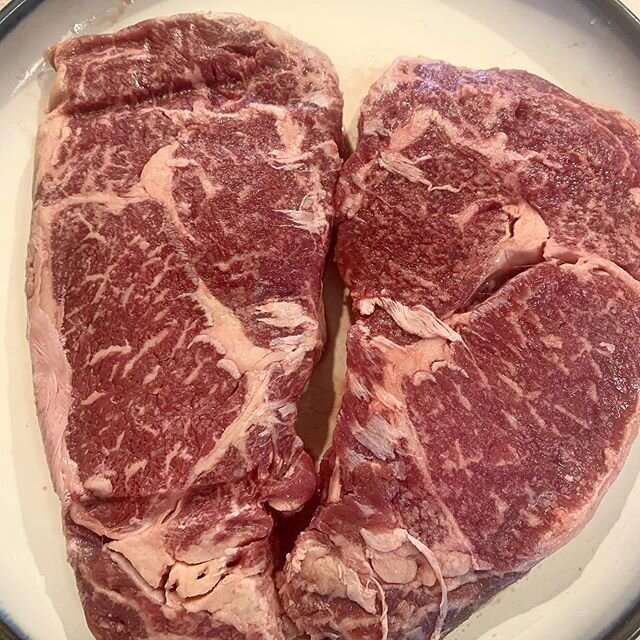 image-asset - 2026-07-17T142647.116 Two raw ribeye steaks showcasing rich marbling and vibrant red color, placed on a white plate, ideal for grilling or pan-searing.