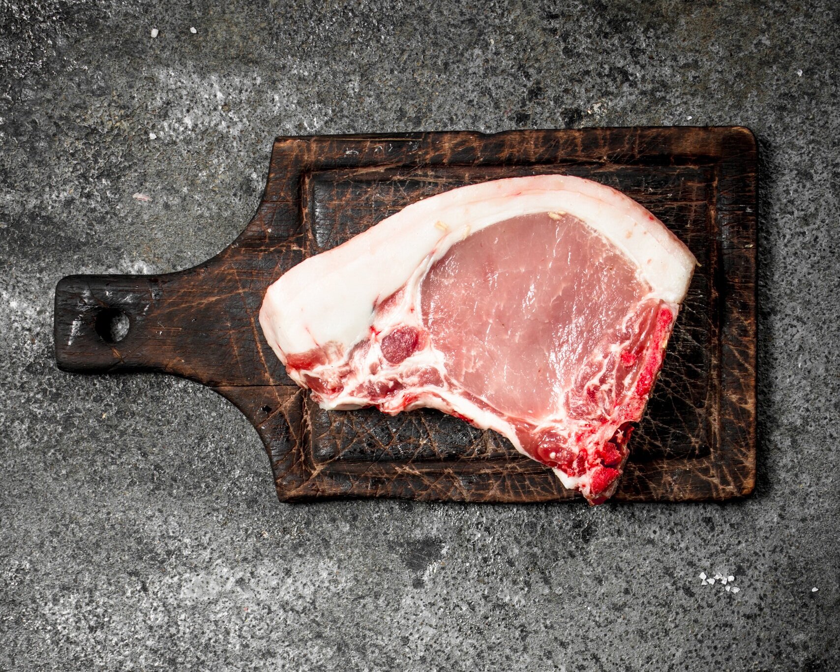 Raw pork chop on a rustic wooden cutting board, showcasing marbling and fat for optimal flavor in cooking.